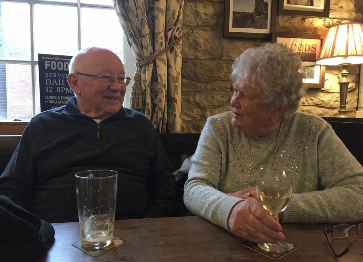 Photorealistic Older Couple in a Pub のQwen Imageプロンプト例 バリエーション 2: Generates a highly realistic portrait of an older couple enjoying drinks and snacks at a warmly lit pub table.
