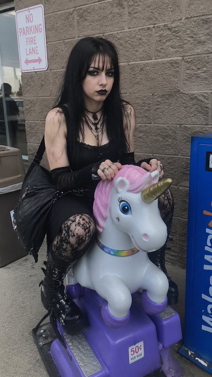Goth Girl on Unicorn Ride Qwen Image 프롬프트 예시: Generates a realistic, candid photo of a goth girl sitting on a children's coin-operated ride outside a store.