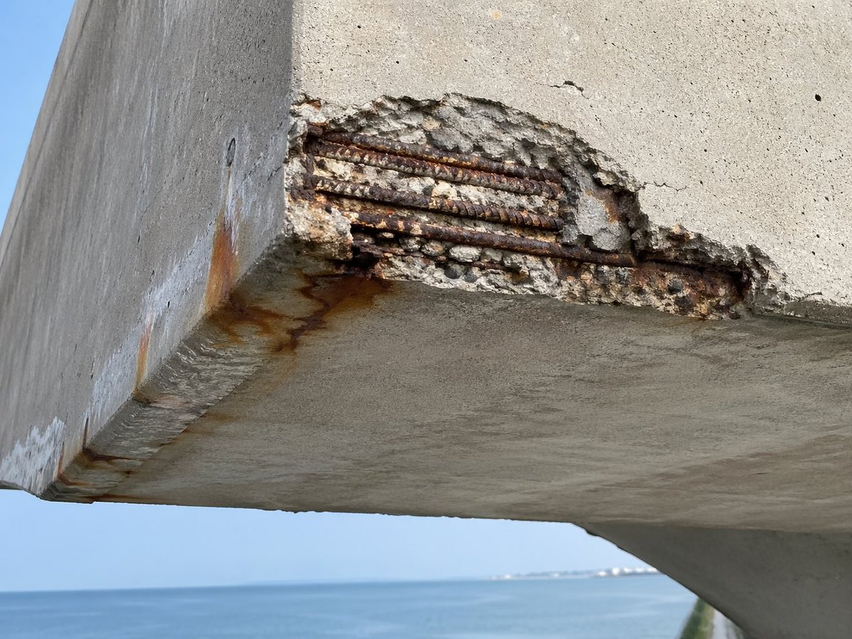 Coastal Reinforced Concrete Salt Damage のQwen Imageプロンプト例: This prompt generates a realistic inspection-style photo of chloride corrosion and concrete spalling on a seaside...