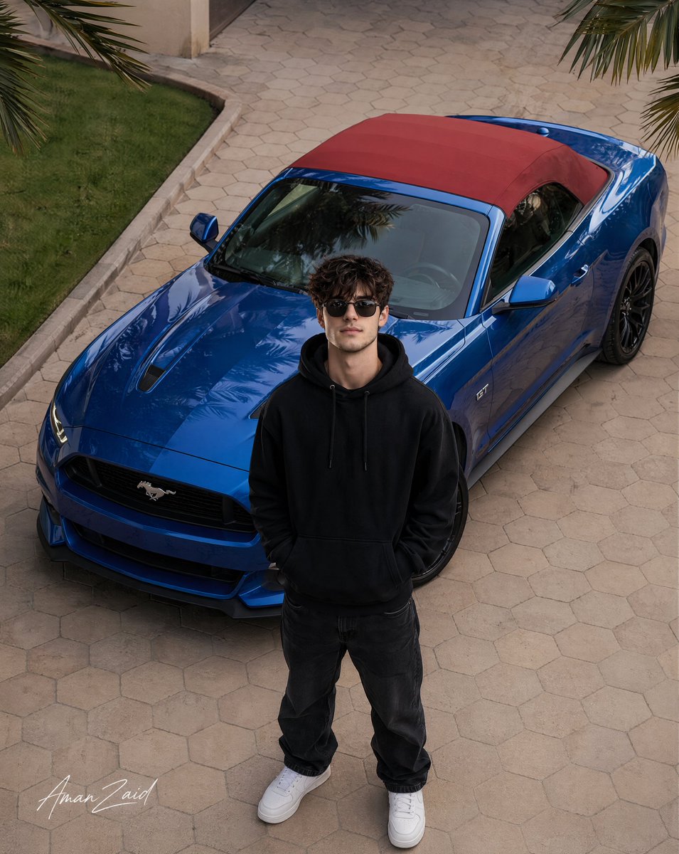 Cinematic portrait of a man with a Ford Mustang Qwen Image prompt example: A comprehensive hyper-realistic prompt for a high-angle aerial photograph of a stylish young man posing...