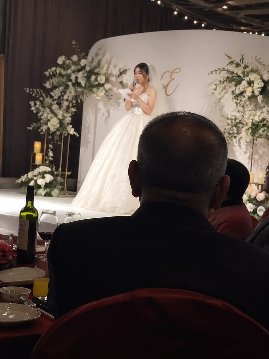 Candid wedding speech photo のQwen Imageプロンプト例: A prompt for a candid, iPhone-style photo of a wedding speech, capturing the emotion of the bride on stage and her father in the...