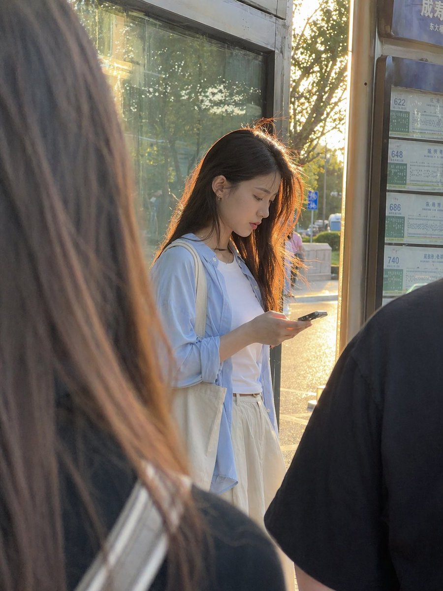 Golden Hour Bus Stop Candid Qwen Image prompt example: This prompt generates a realistic candid urban portrait of a young woman at a bus stop, ideal for lifestyle photography and...