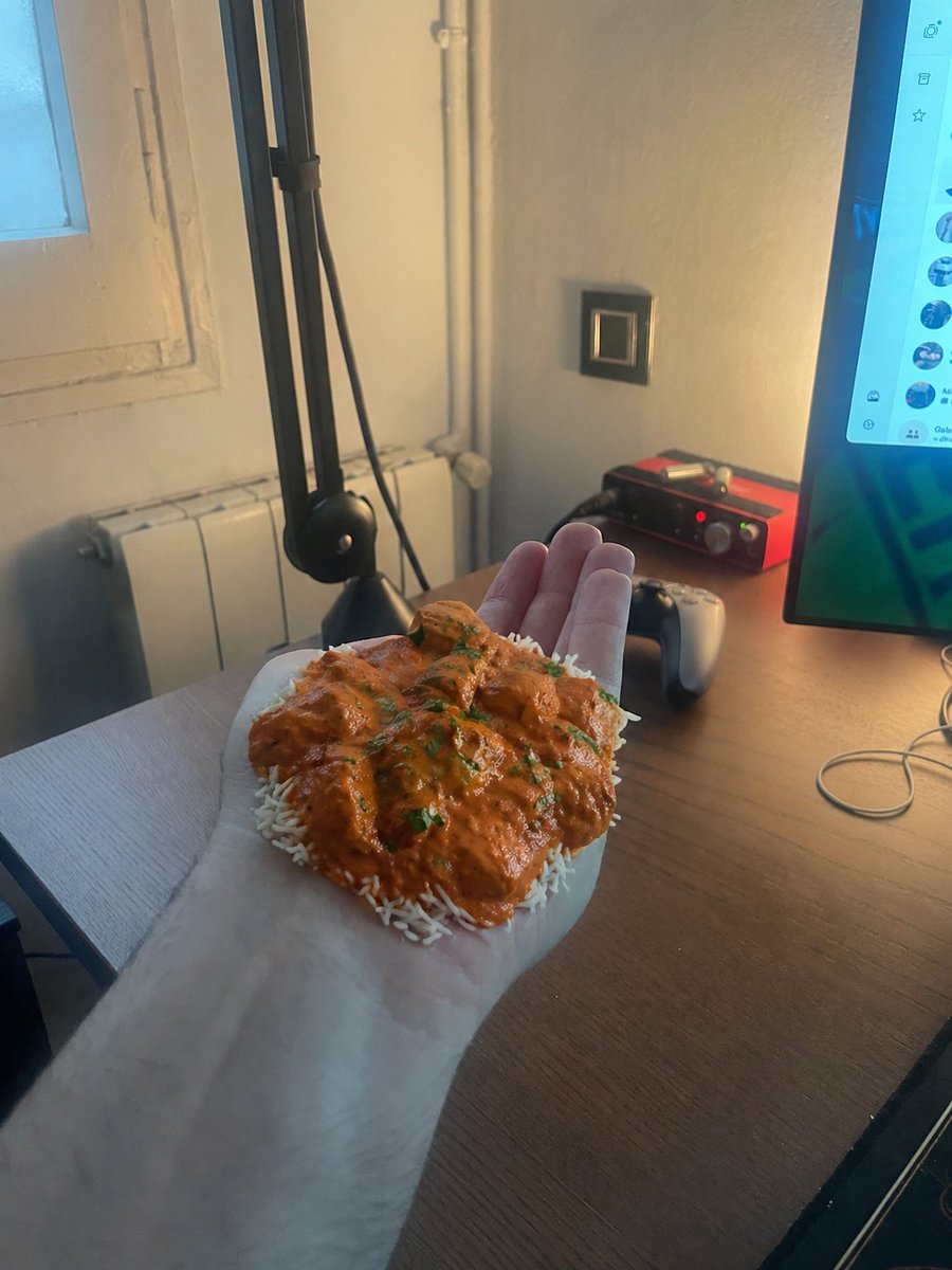 Chicken Tikka Masala Mug Desk Photo のQwen Imageプロンプト例 バリエーション 2: A photorealistic joke snapshot of a hand holding a black mug filled with chicken tikka masala in a warm-lit desk...