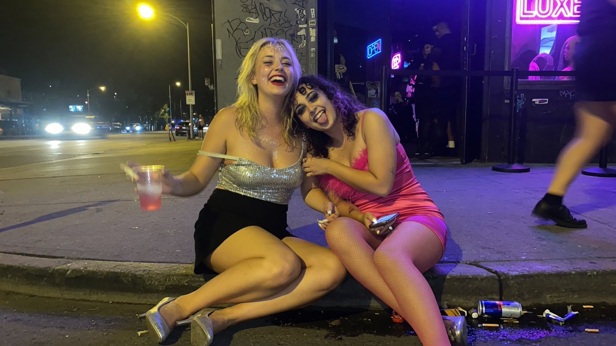 Candid Nightclub Curb Scene Qwen Image prompt example: Generates a photorealistic late-night urban party snapshot of two anonymized women sitting on a curb outside a neon...